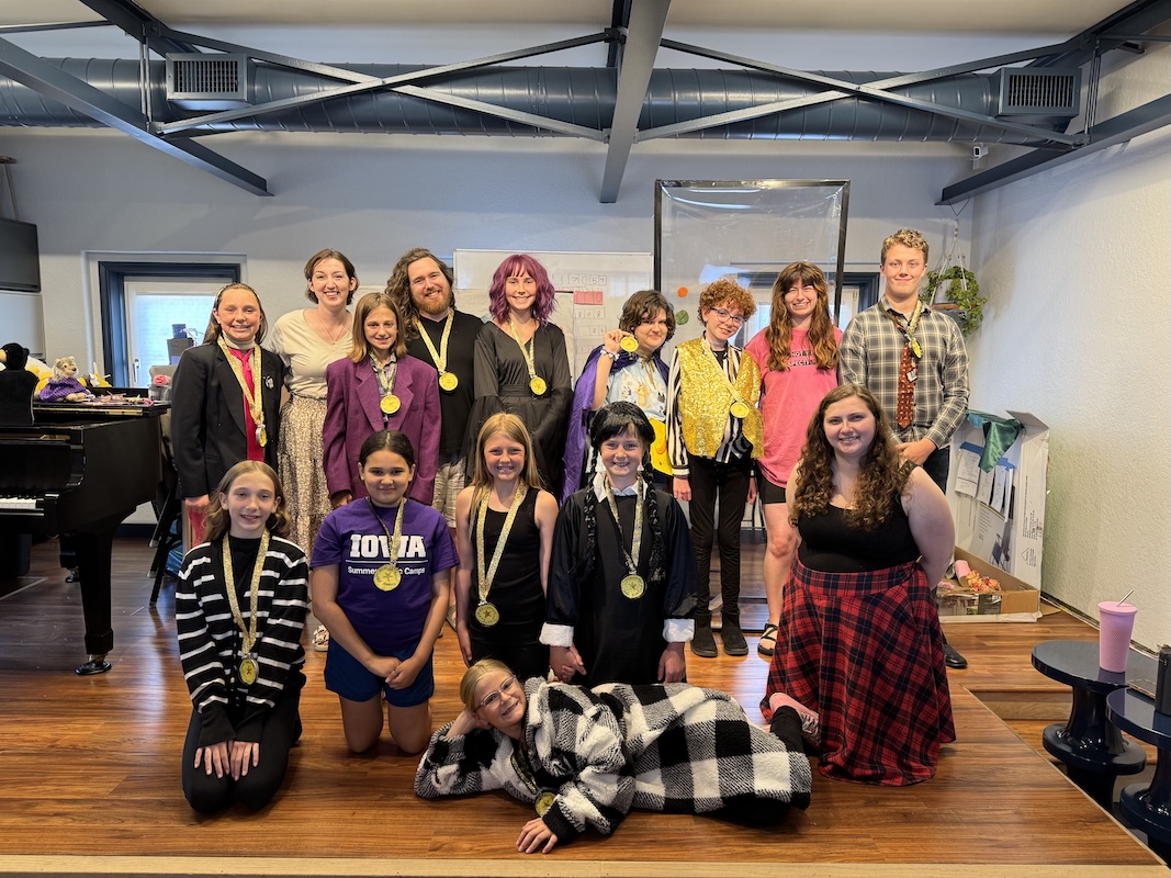 Group of music students and instructors standing together in a studio, smiling and wearing medals after a performance or event.