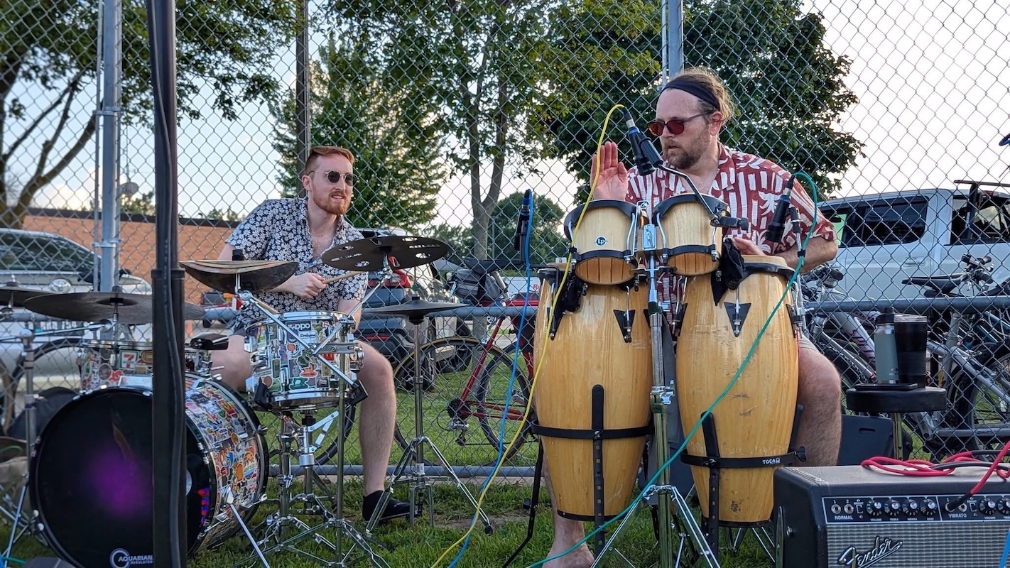 Music instructors playing drums and congas during an outdoor jam session at Lott Music Studio.