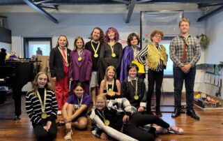 Middle school students wearing medals pose together on a stage during Lott Music Studio summer camp.
