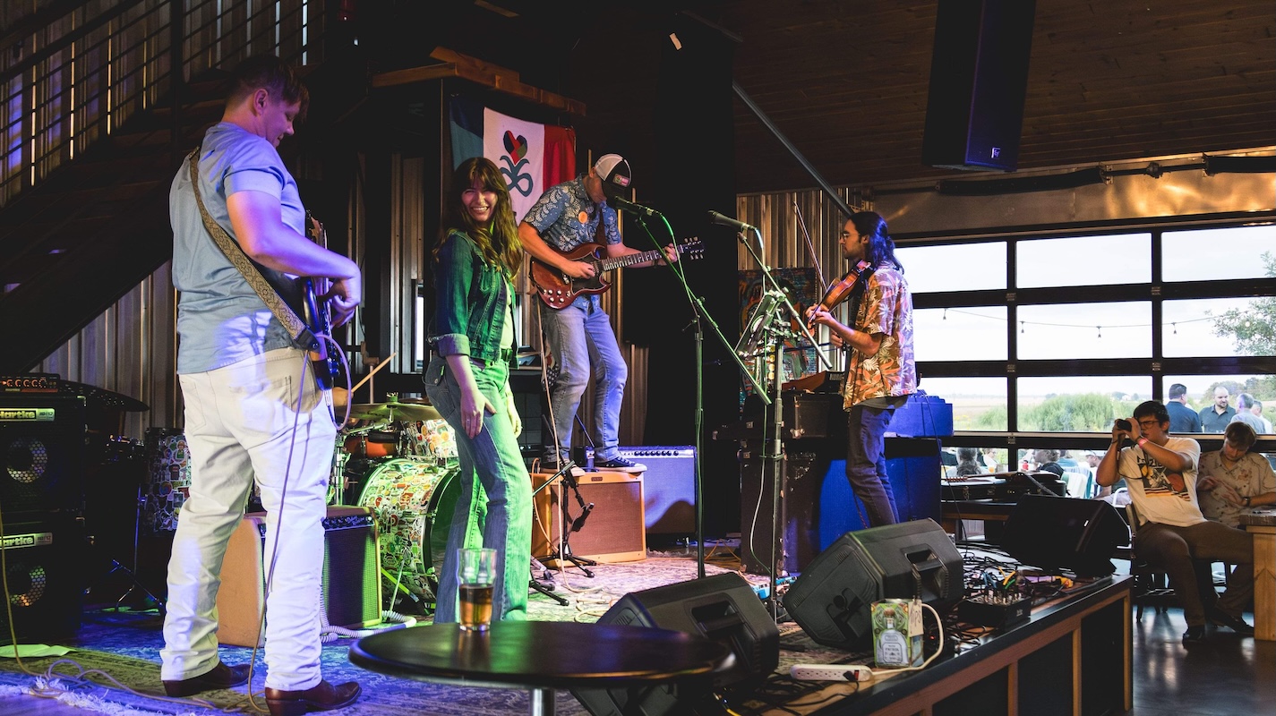 Music instructors performing live with guitar, violin, drums, and vocals during a Lott Music Studio jam session.