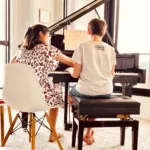 A piano instructor giving a one-on-one music lesson during the back-to-school season at Lott Music Studio.