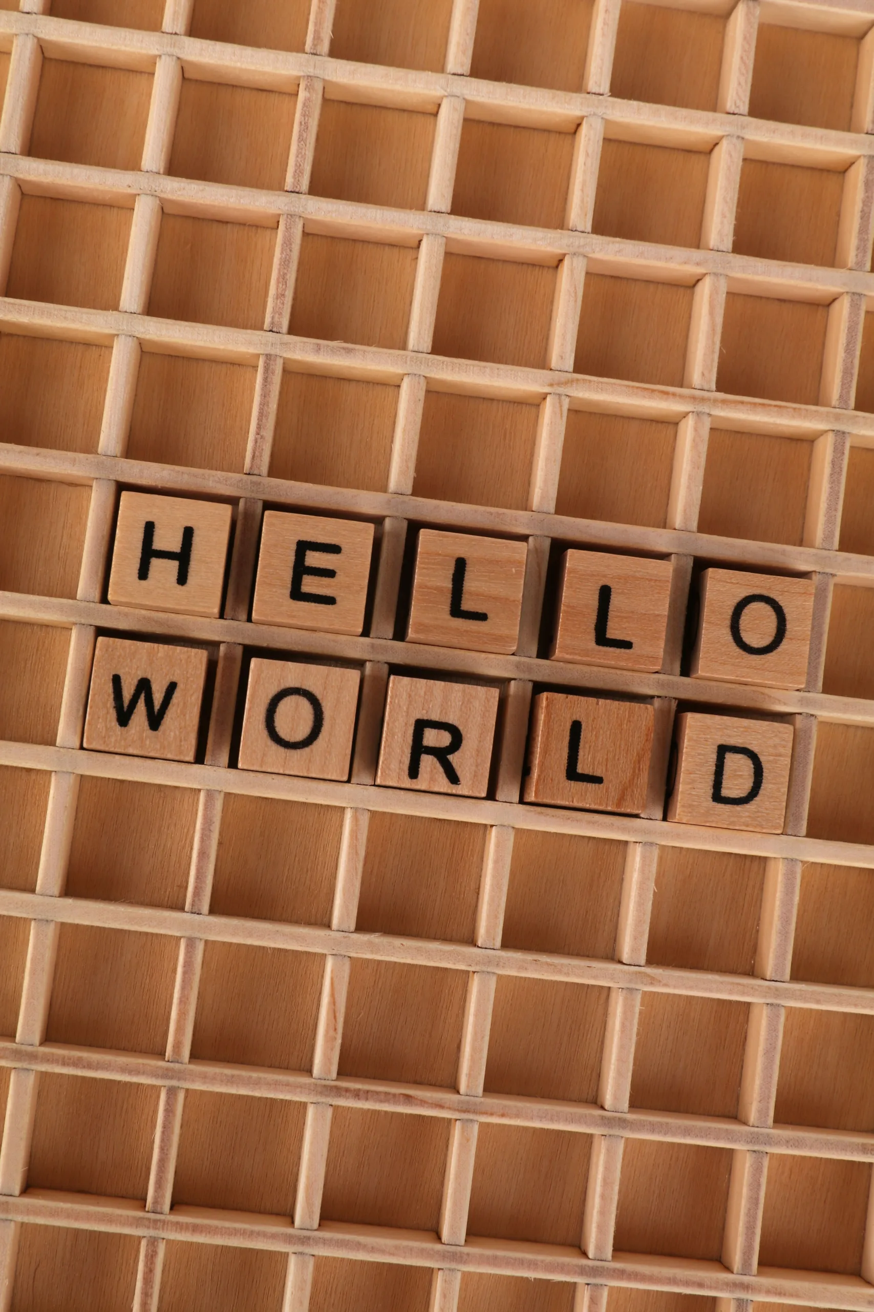 The phrase "Hello World" spelled out using wooden Scrabble tiles on a game board.